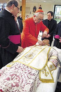 'Monsignor George Tomichek (left) who has been at each opening of St. John Neumann’s casket since 1962, watches Justin, Cardinal Rigali adjusting the saint’s new vestments. Monsignor John McIntyre (right) along with Auxiliary Bishop Joseph Cistone, Fathers Kevin Moley & Patrick Woods, and Monsignor Daniel Sullivan (not pictured) also attended the solemn and moving event.'