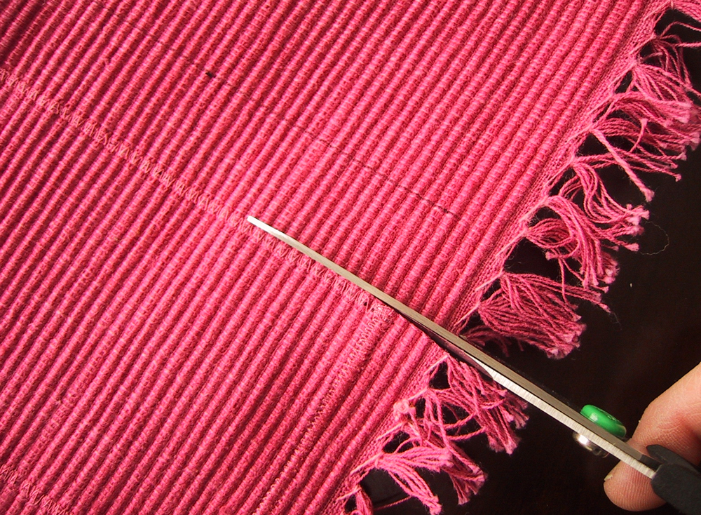 Scissors cutting along a line of zig zag stitch on a pink woven place mat.