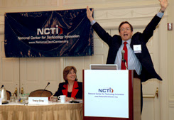 Tracy Gray, seated, Jim Fruchterman with both hands over his head at a podium